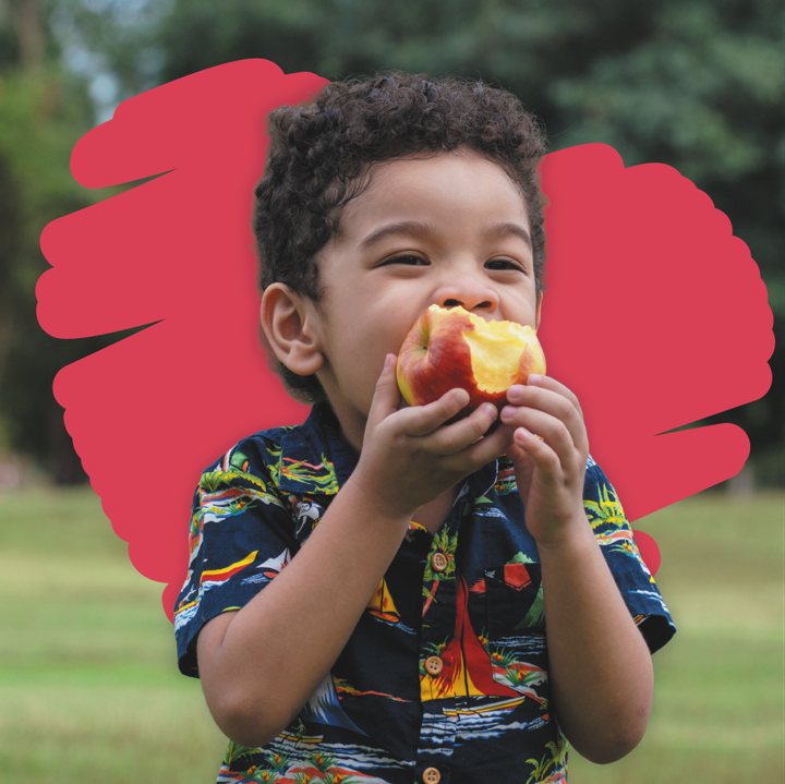 A young boy smiling while eating a peach